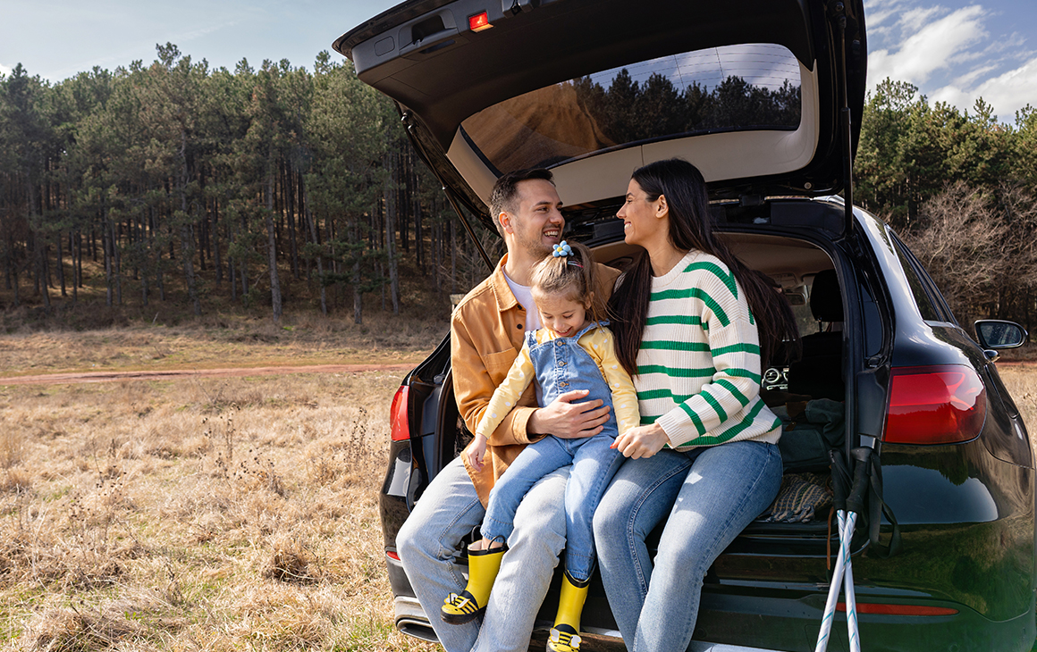 Família sorridente a viajar de carro junto à praia.